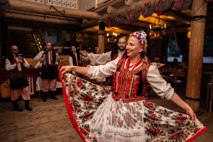 Woman in traditional dress dancing with musicians in background in a rustic setting.