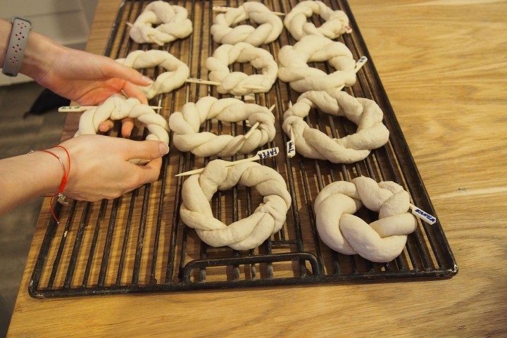 Hands shaping pretzel dough on a cooling rack with several unbaked pretzels.