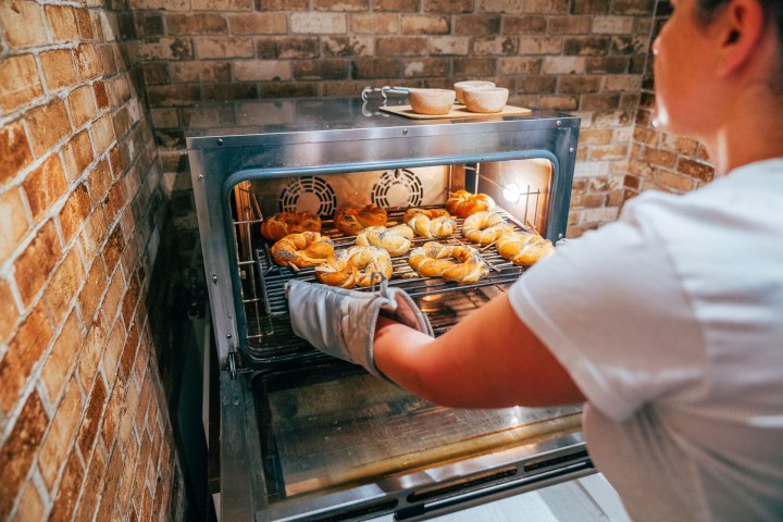 Person placing baked pastries into a brick oven.
