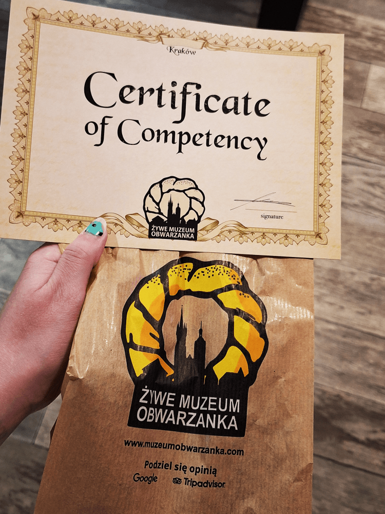 Hand holding a certificate and a brown bag with a pretzel logo.