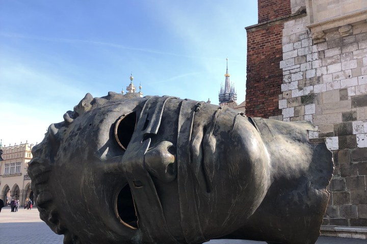 Large bronze head sculpture lying on its side in a plaza.