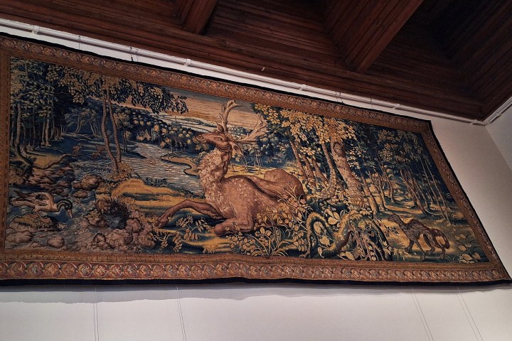 Intricate tapestry with a deer and forest scene on a wall.