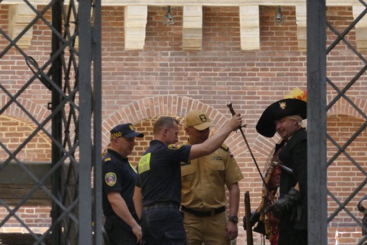 Three costumed men with guitars and two uniformed officers indoors.