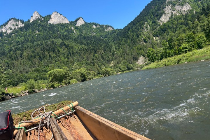 Wooden boat on a river with forested mountains in the background under a clear blue sky.