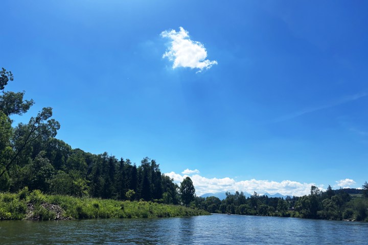 River flowing through green landscape under bright blue sky with a single cloud.
