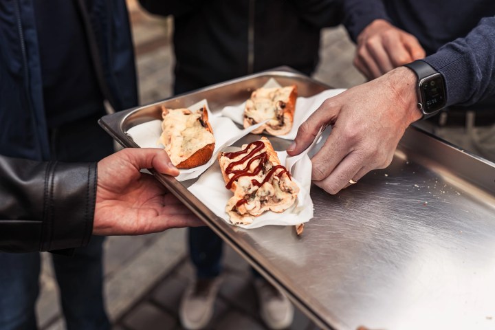 Hands holding a tray of sausage rolls on napkins.