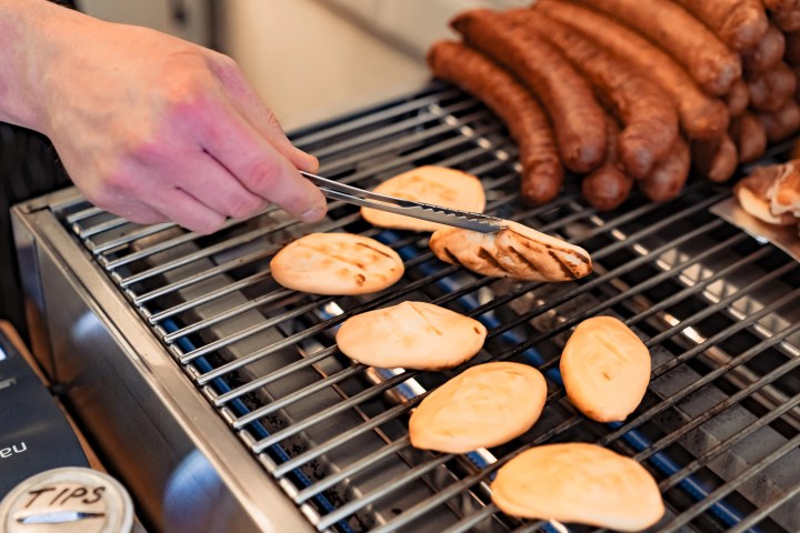 Person grilling sausages and flatbreads on a barbecue grill.