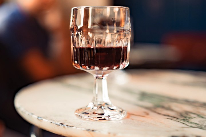 Glass of red wine on a wooden table, blurred person in the background.