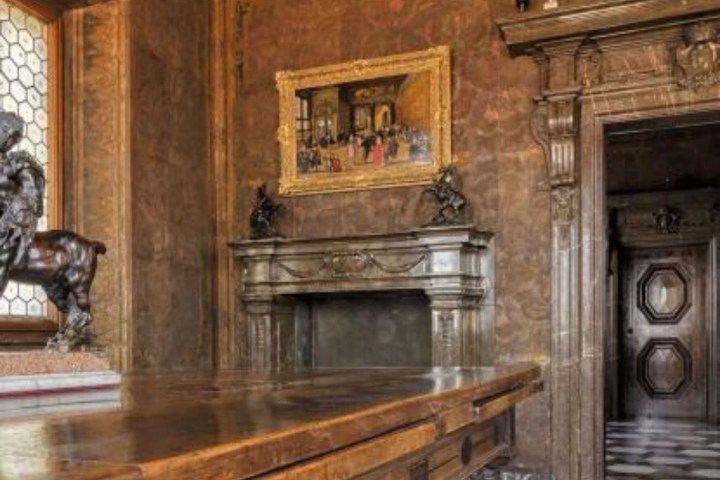 Ornate room with wooden table, fireplace, framed art, and decorative ceiling.
