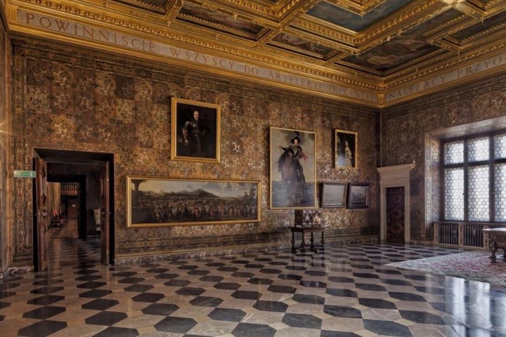 Ornate room with checkered floor, paintings on walls, and large window.
