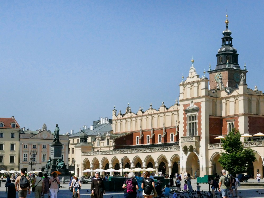 People walk by a historic building with arches and a tower in a European square.