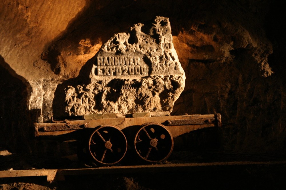 Rustic metal cart with 'HANNOVER EXPO 2000' rock in underground cave setting.
