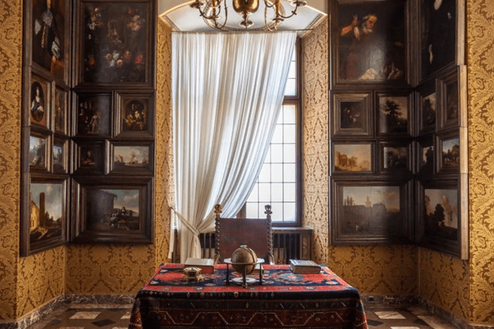 Ornate room with paintings, a desk, and statues on columns.