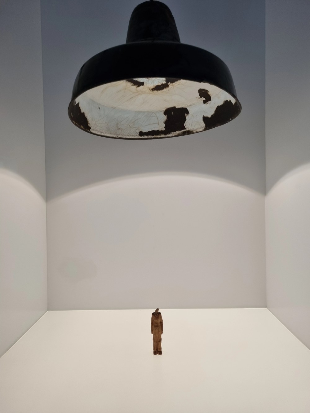 Tiny statue under large, worn-out ceiling light in a minimal room.
