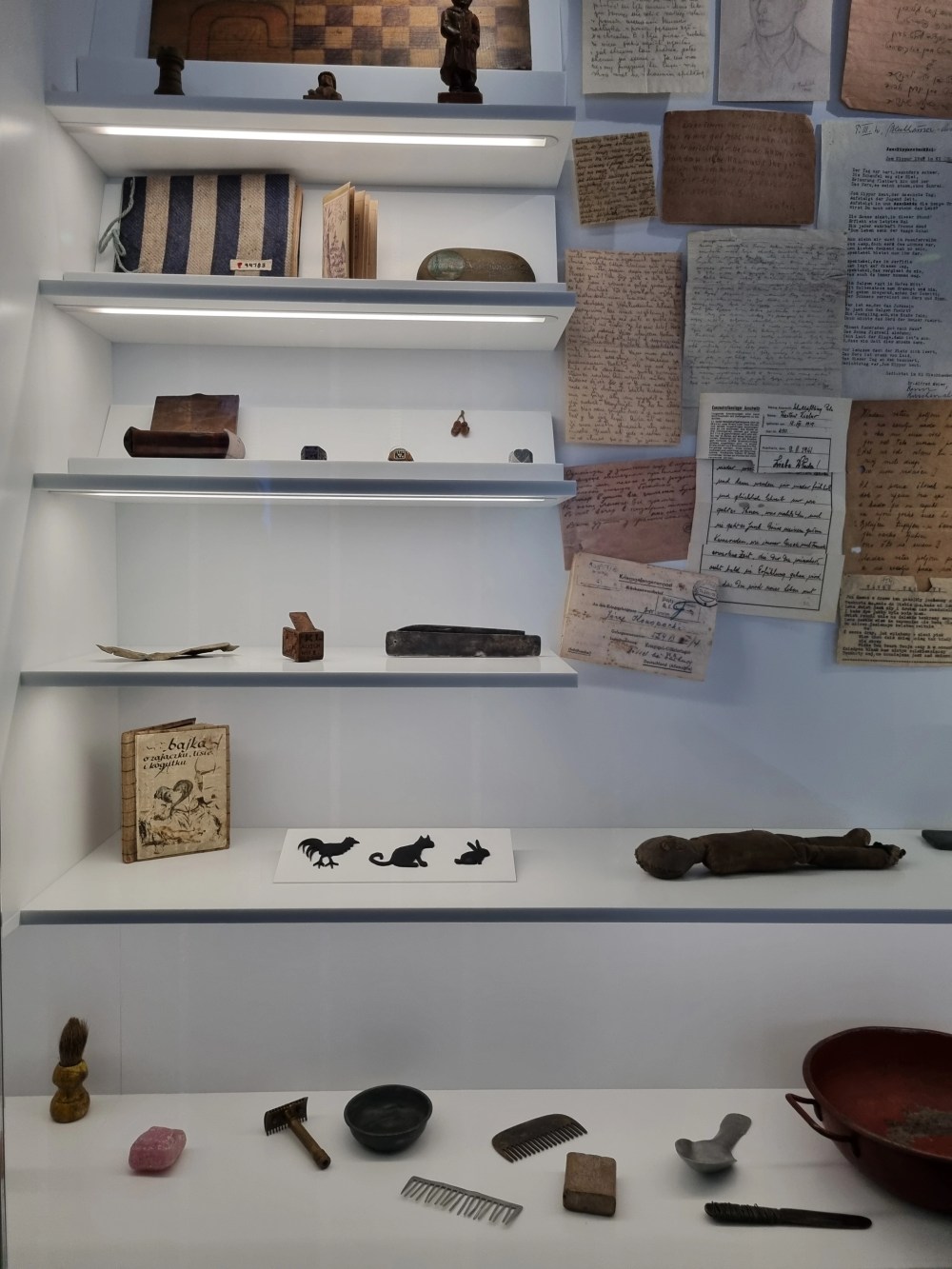 Museum display with books, trinkets, papers, and small artifacts on shelves.