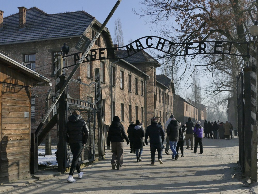 People walking under the Auschwitz gate with the sign 'Arbeit Macht Frei'