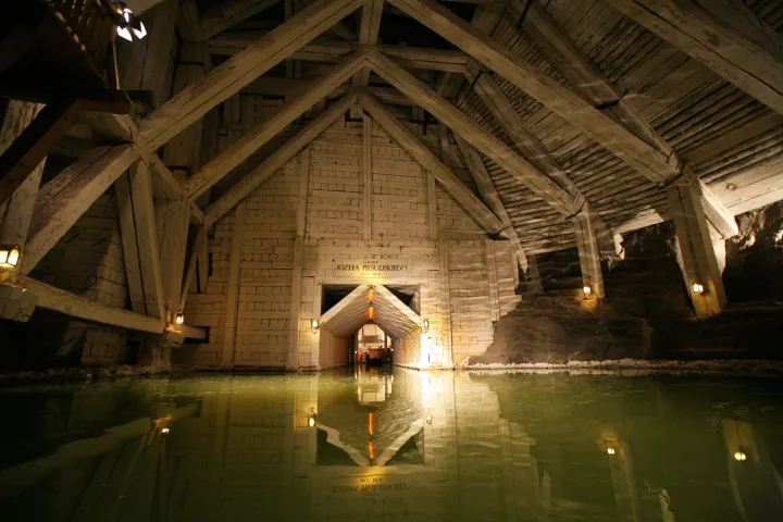 Underground salt mine chamber with green water and wooden beams.