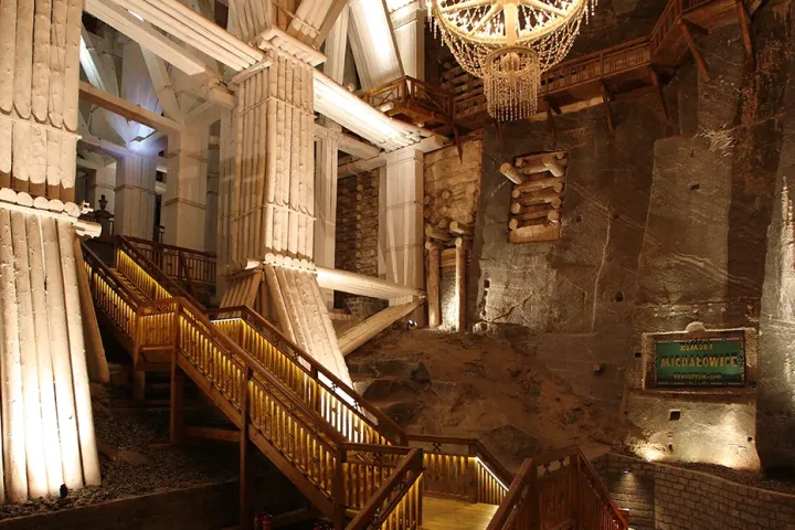 Grand wooden staircase in an underground hall with chandeliers.