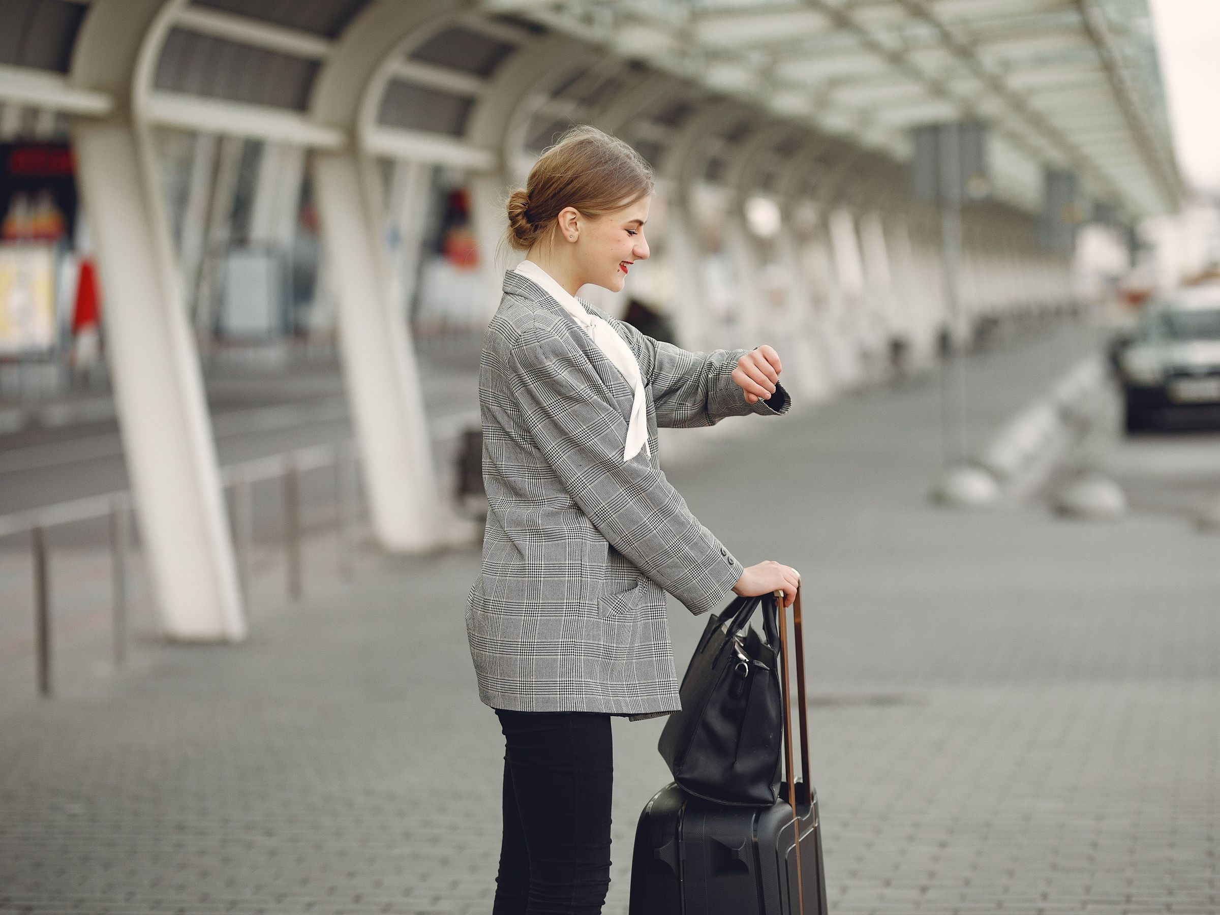 Woman in a gray coat waiting at a train station with a suitcase.
