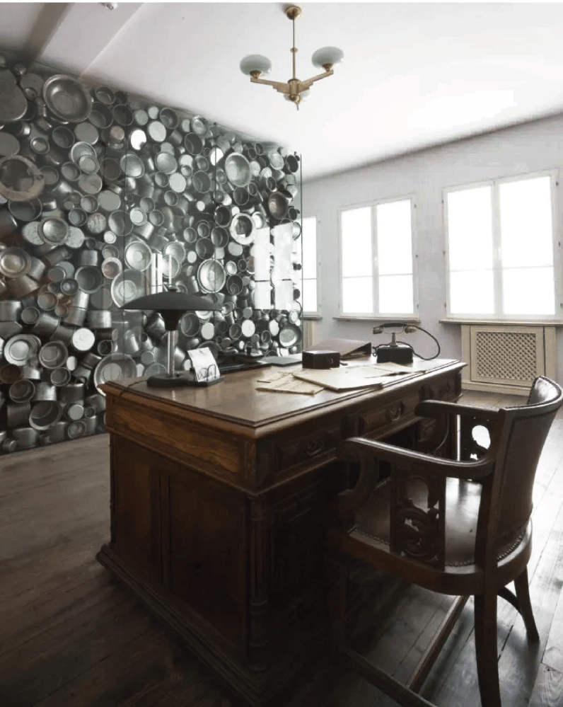 Office with wooden desk, chair, and a wall covered in metal pots and pans.