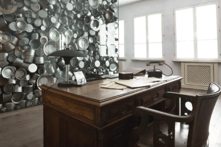 Office with wooden desk, chair, and a wall covered in metal pots and pans.