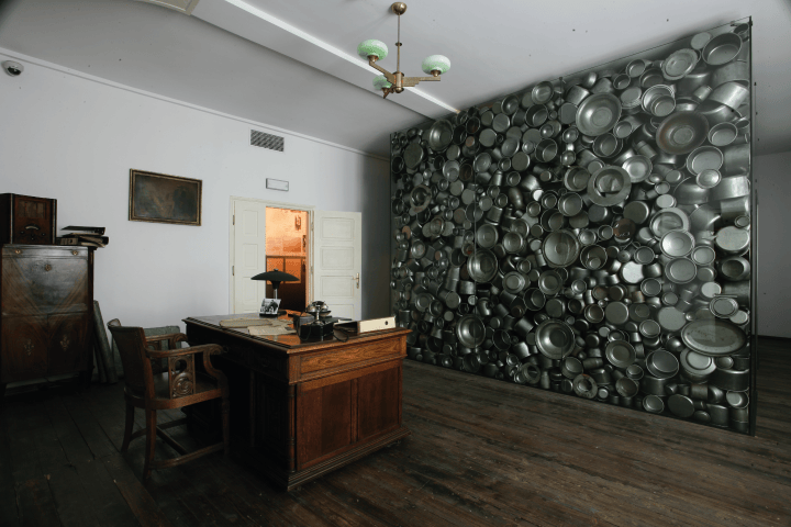 Room with wooden desk, chair, and wall covered in metal pots and pans.