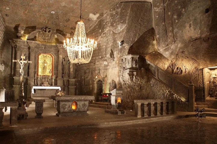 Ornate underground chapel with chandelier, altar, carvings and stone walls.