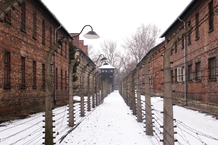 Snowy path between barbed wire fences and brick buildings.