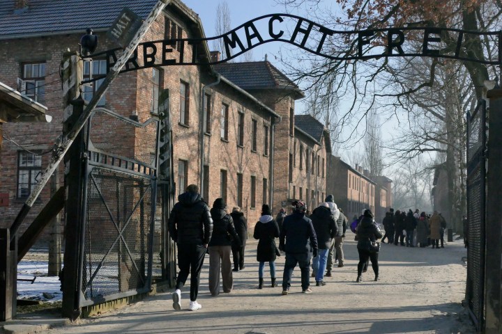 Visitors walking through a gate under a sign at a historical brick building site.