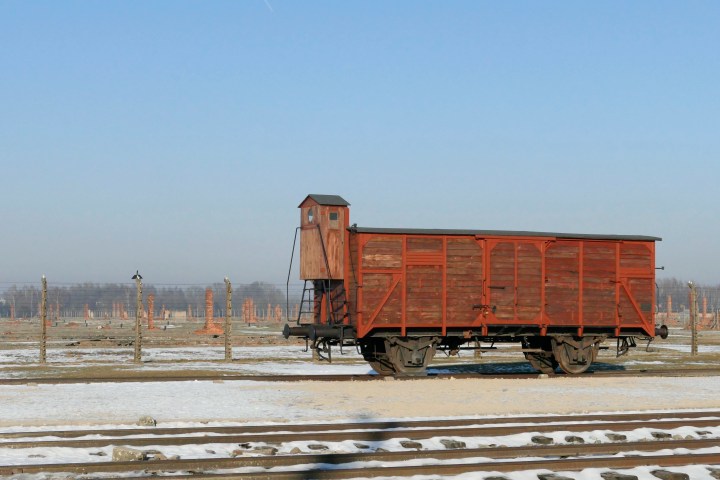 Old wooden train car on snowy tracks with clear blue sky.