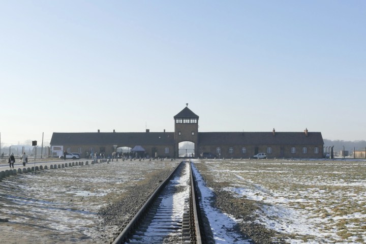Rail tracks leading to a large brick gate building at a historical site on a clear day.