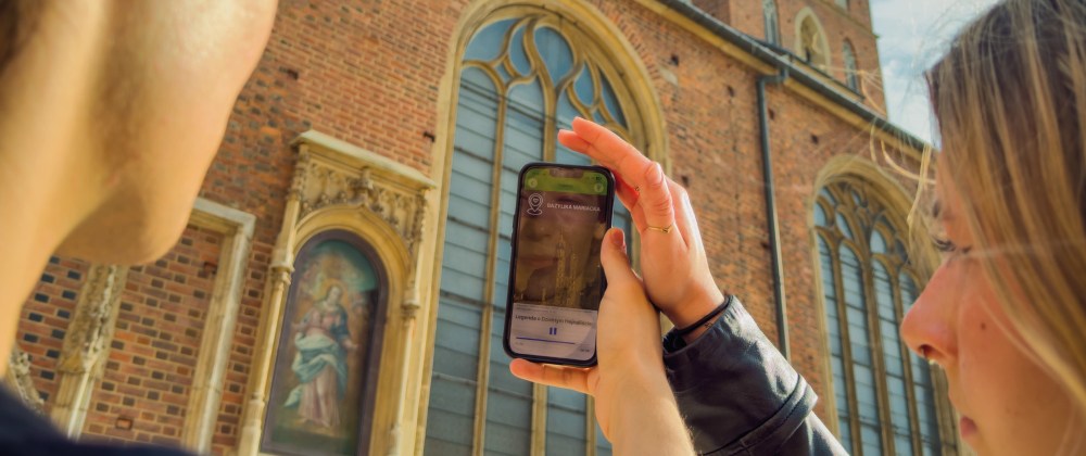 Two people outside, one taking a photo of a church with tall arched windows using a smartphone.