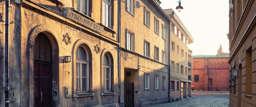 Sunlit narrow street with old buildings and a star of David on one facade.