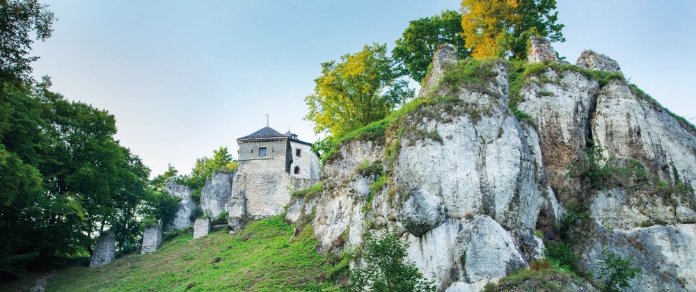 Stone building on a rocky hilltop surrounded by green trees.