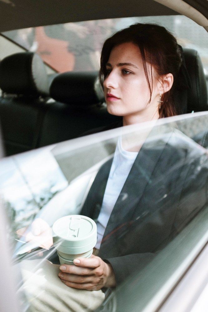 Woman sitting in a car holding a cup, looking out the window.
