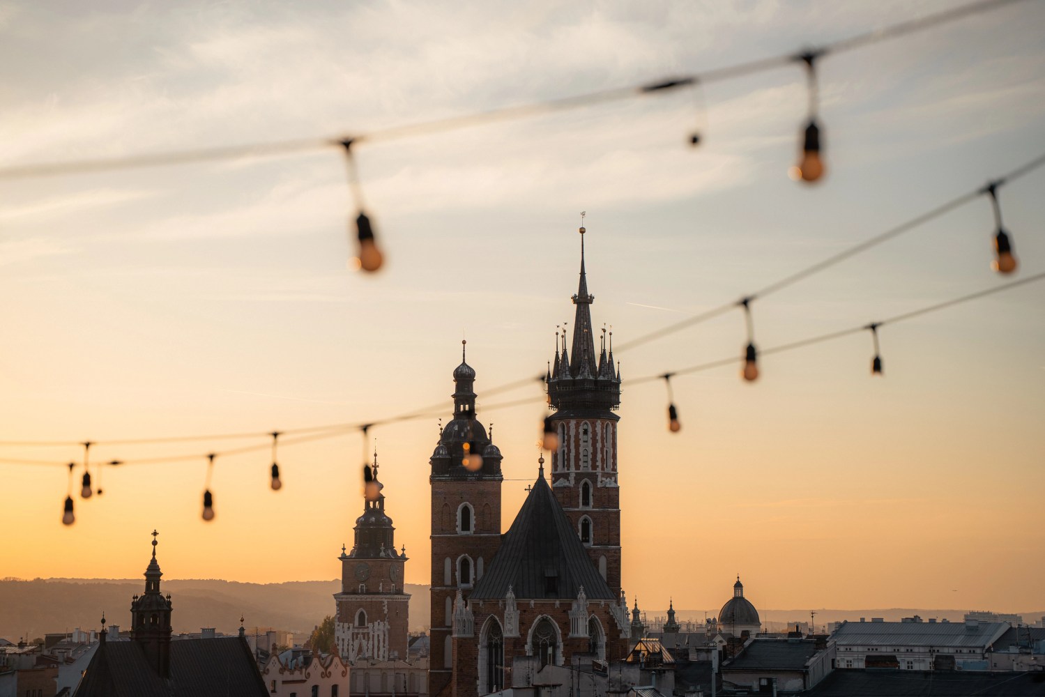 String lights hang over a city skyline with historic towers at sunset.