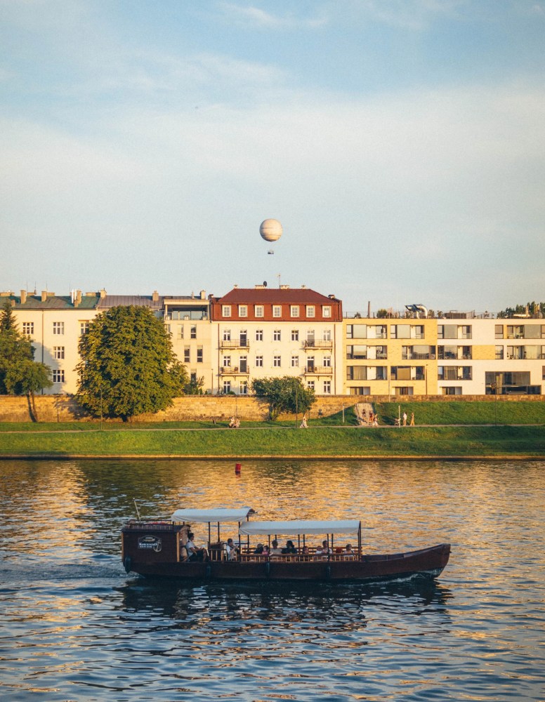 Boat on river with buildings and a balloon in the background.
