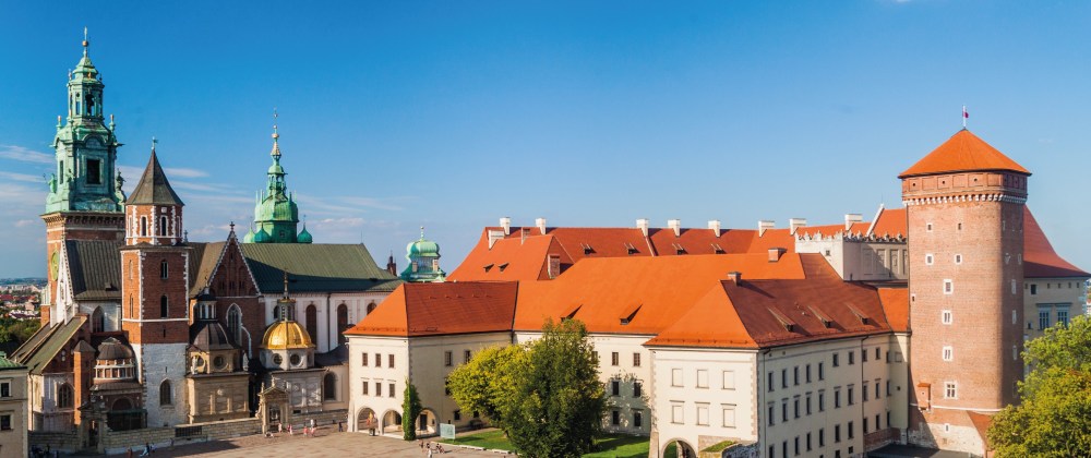 Historical castle complex with red roofs and towers under a clear blue sky.