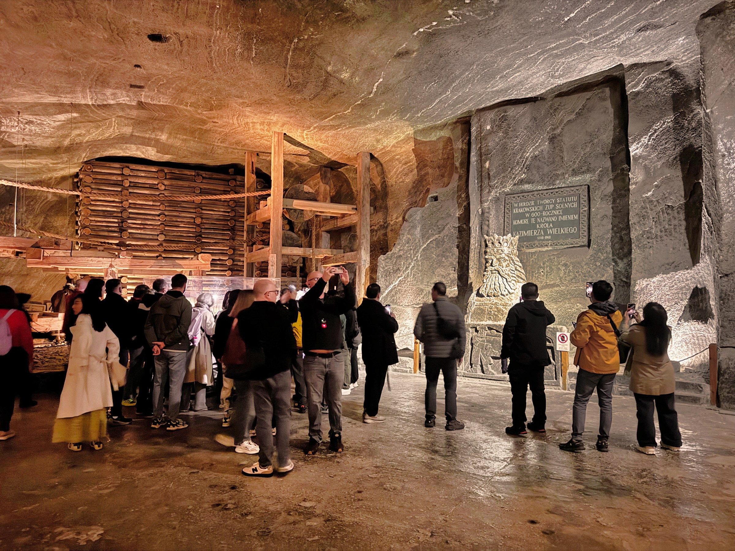 Tour group in a large, dimly lit stone cave examining a wall display.