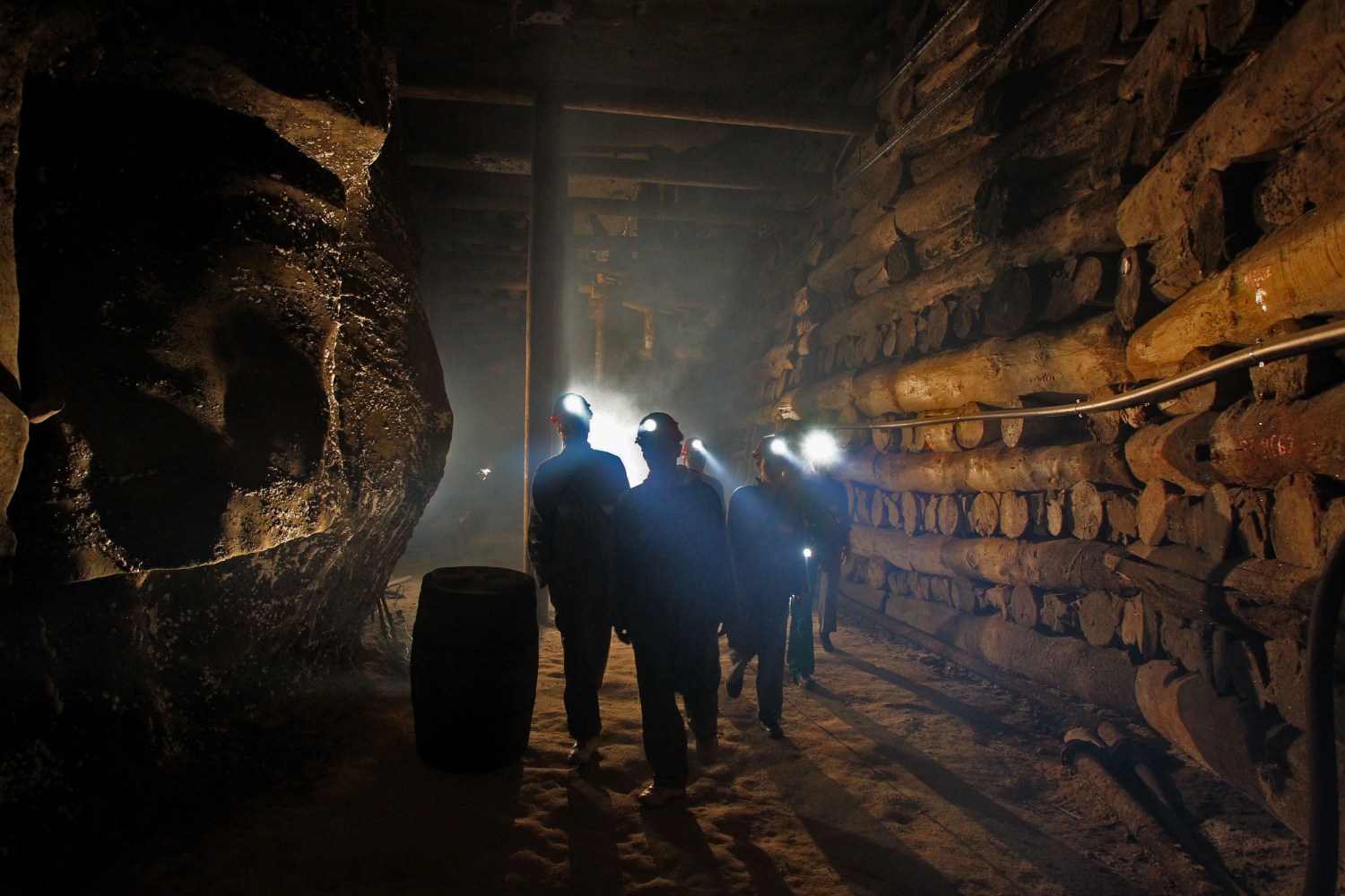 People with helmets explore dimly lit underground cave or mine with wooden supports.