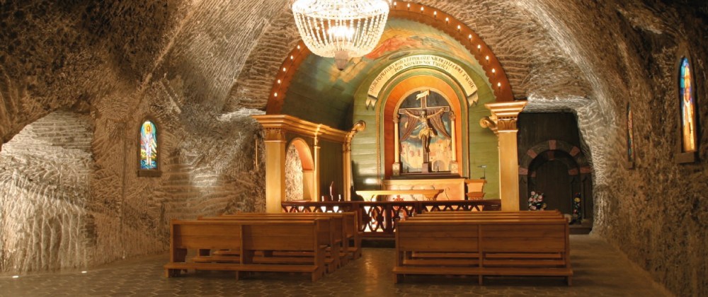 Ornate salt mine chapel with benches, a chandelier, and religious artwork.